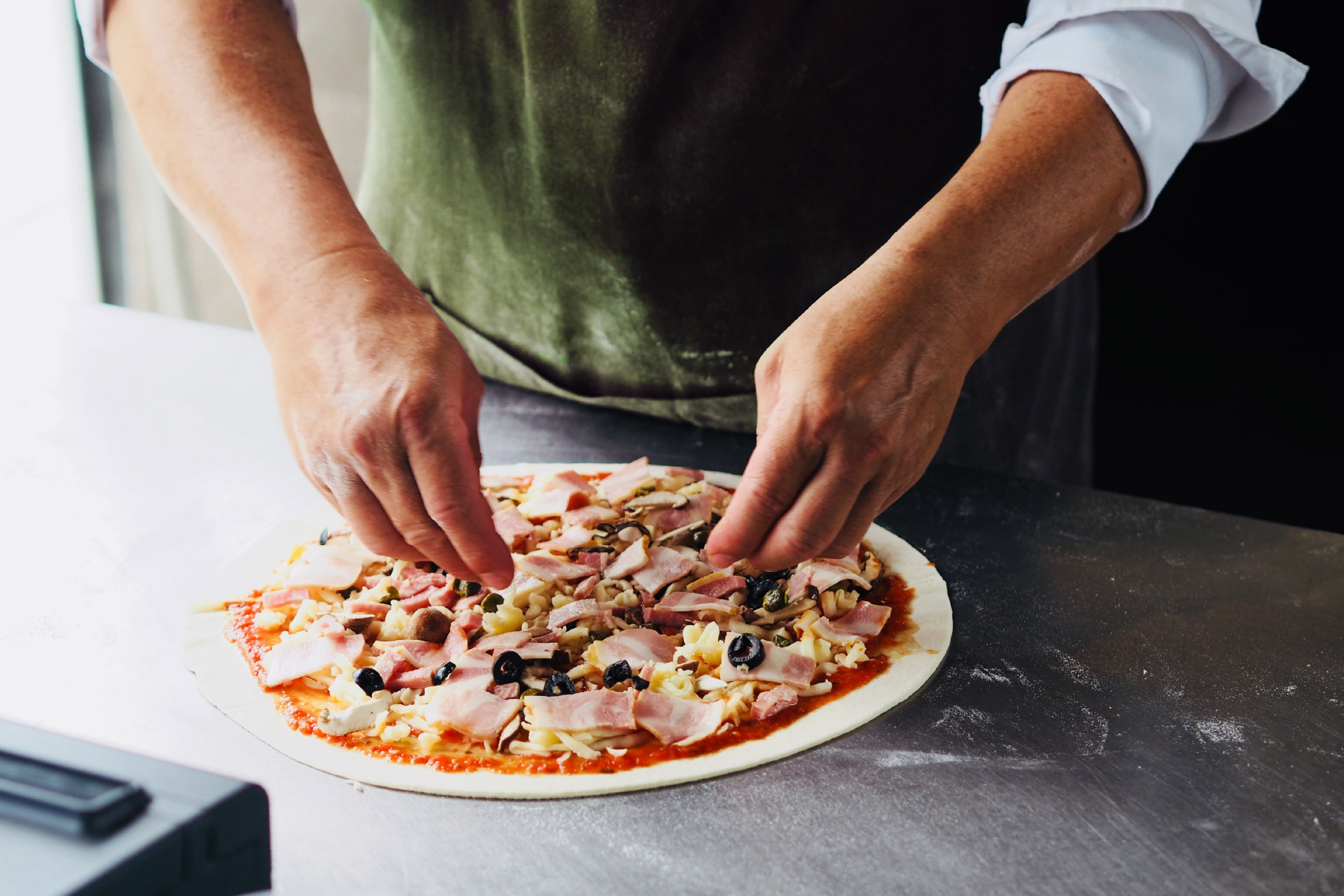 man in green apron preparing a personal pizza with toppings